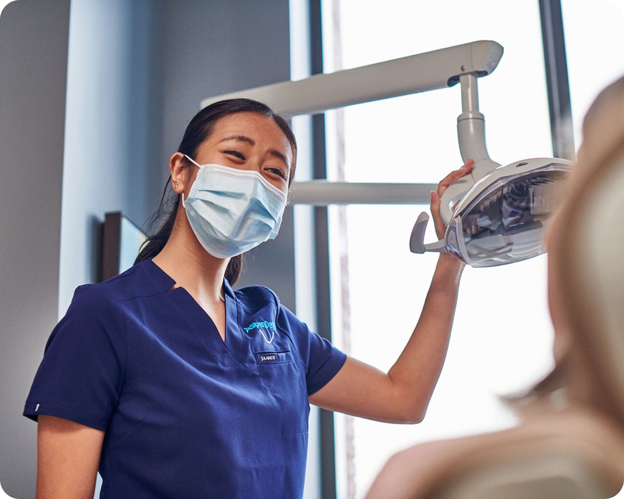 Dental professional wearing a face mask adjusts an overhead dental light while preparing to care for a patient.