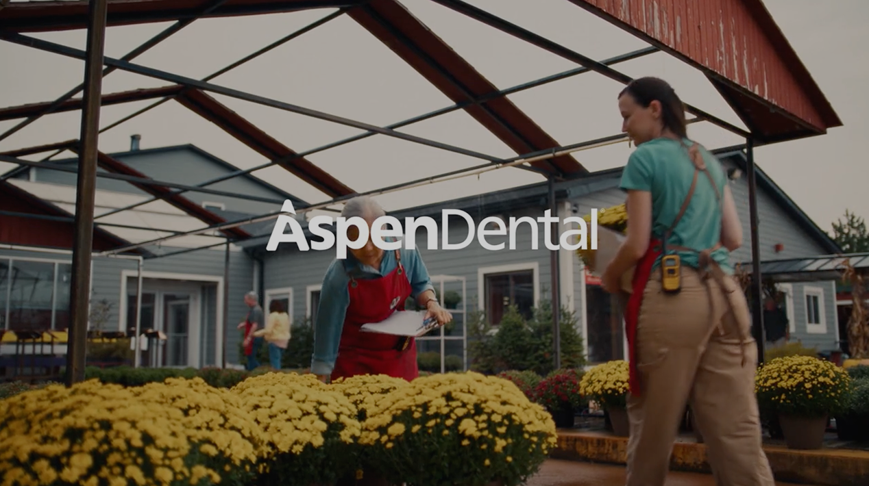 Aspen Dental video thumbnail featuring two women working in a garden center, highlighting real patient smiles and active lifestyles.