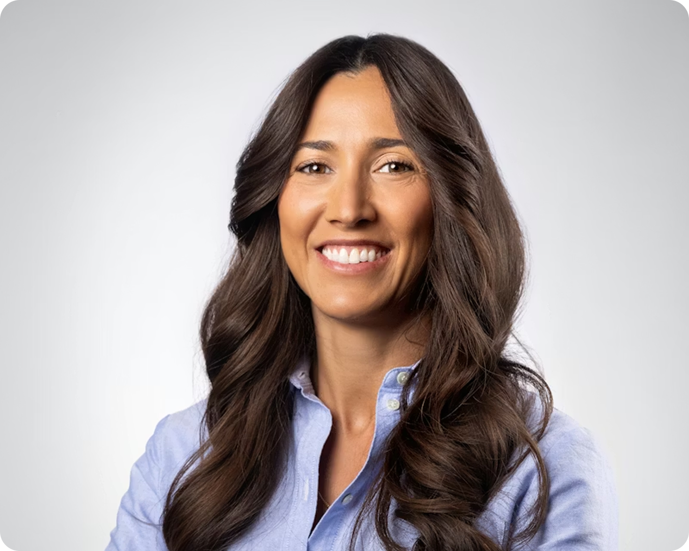 Professional headshot of a smiling woman with long dark hair wearing a light blue blouse against a gray background