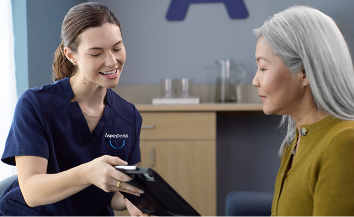 Dental hygienist reviewing treatment plan on tablet with senior female patient during consultation in modern dental office.