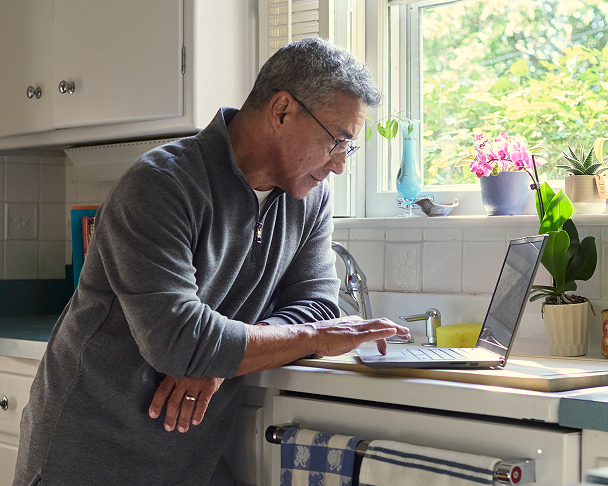 Older man using a laptop at a kitchen counter.