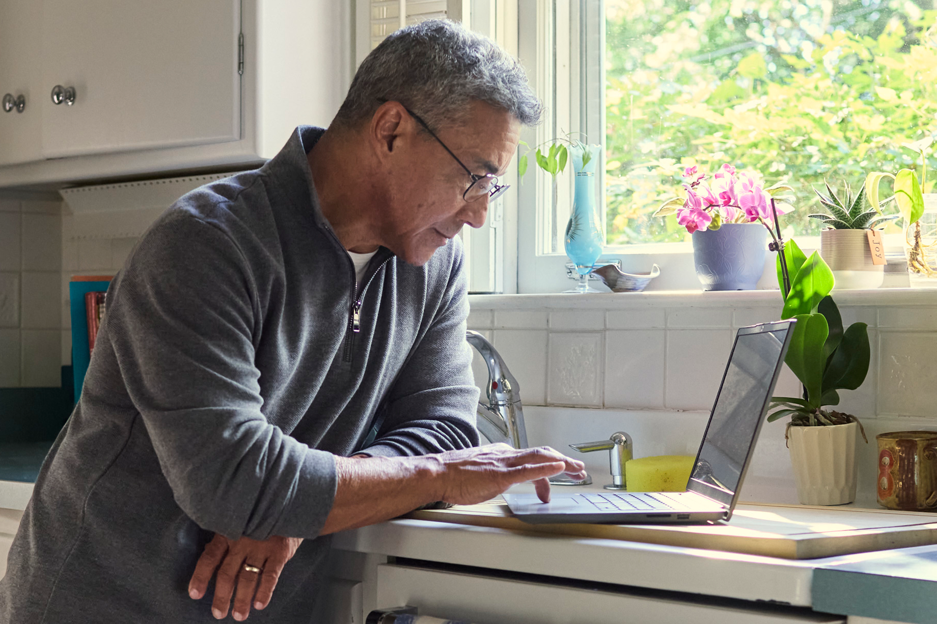Older adult man using a laptop at home, representing research or scheduling related to dental care.