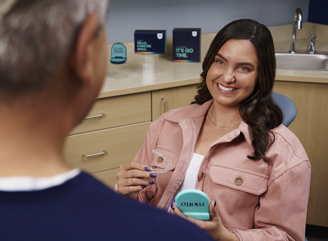 A smiling patient holds clear aligners during a dental visit