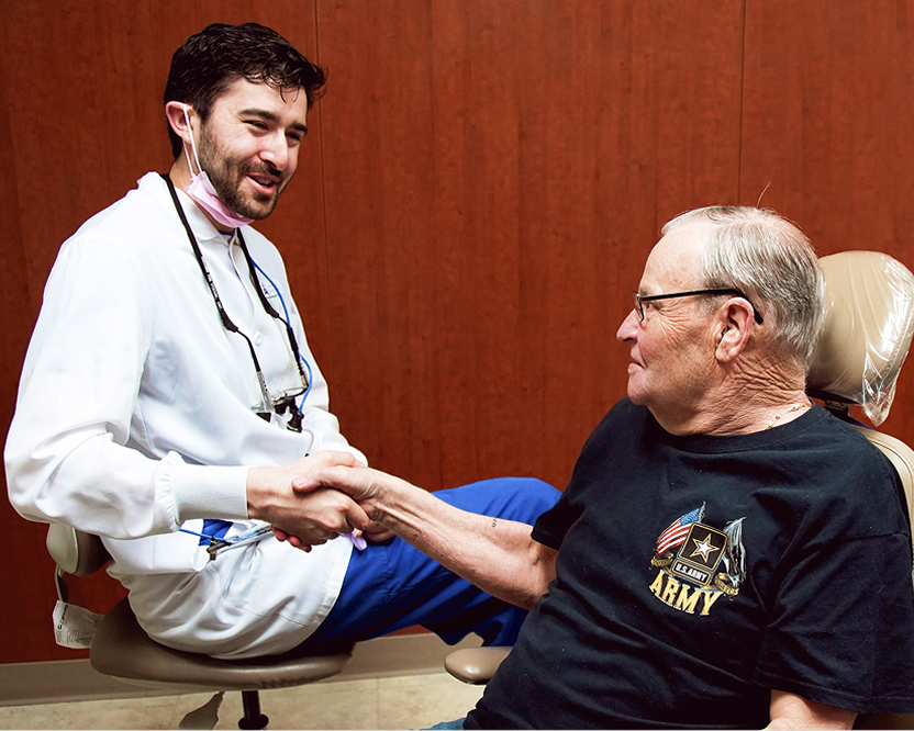 Aspen Dental dentist shaking hands with an older adult man seated in a dental chair after a visit.