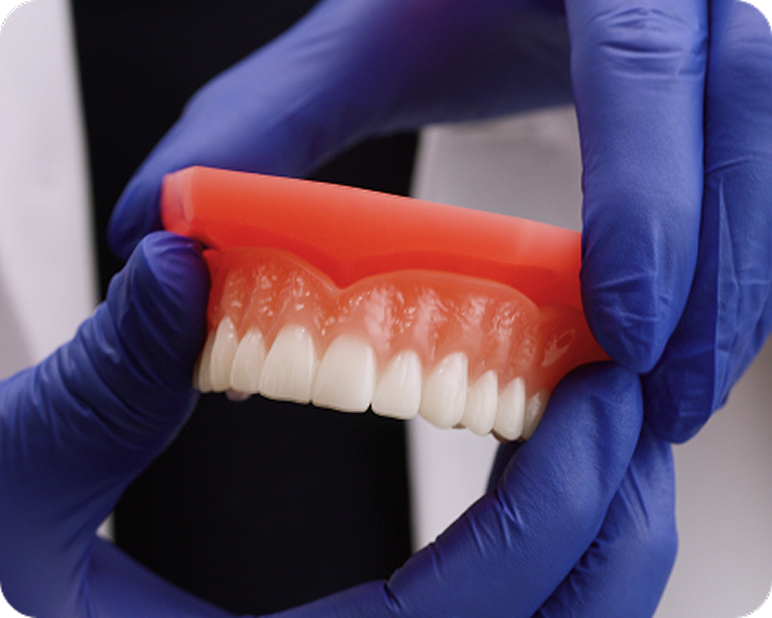 Dental professional holding a denture with gloved hands.
