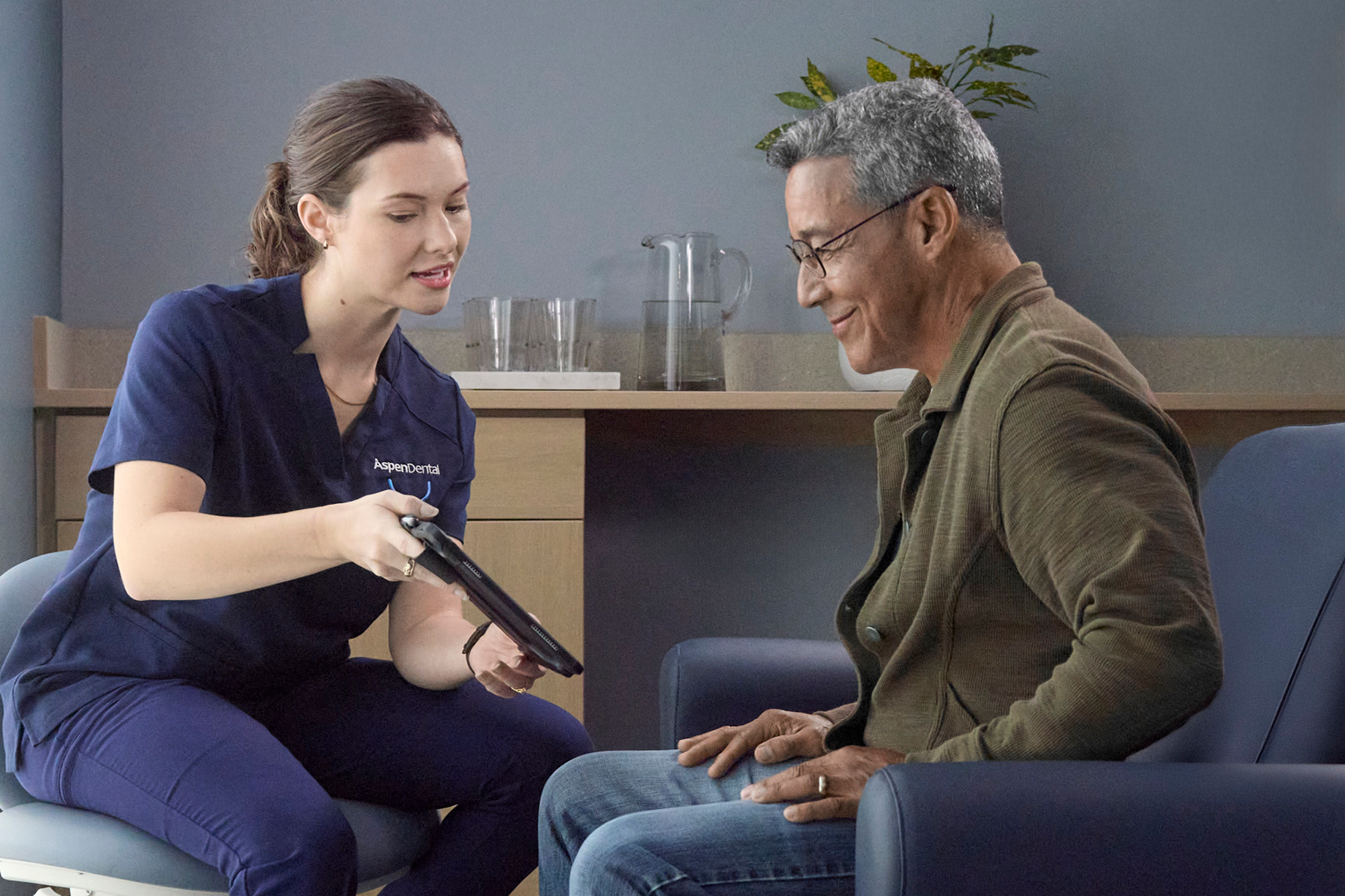 Aspen Dental professional reviewing information on a tablet with an older adult man during a dental consultation.