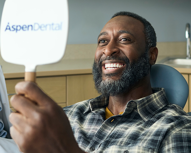 Patient smiling while looking at his teeth in an Aspen Dental mirror.