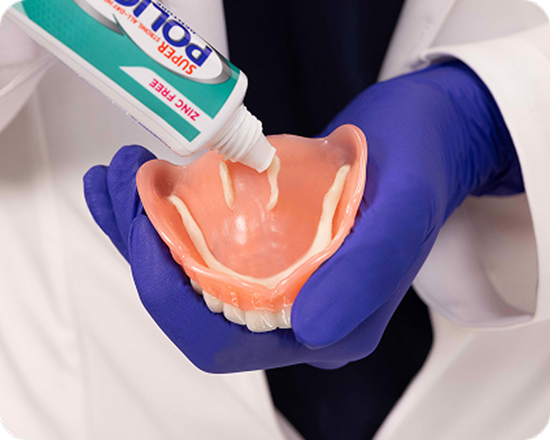 Dental professional applying adhesive to a denture.