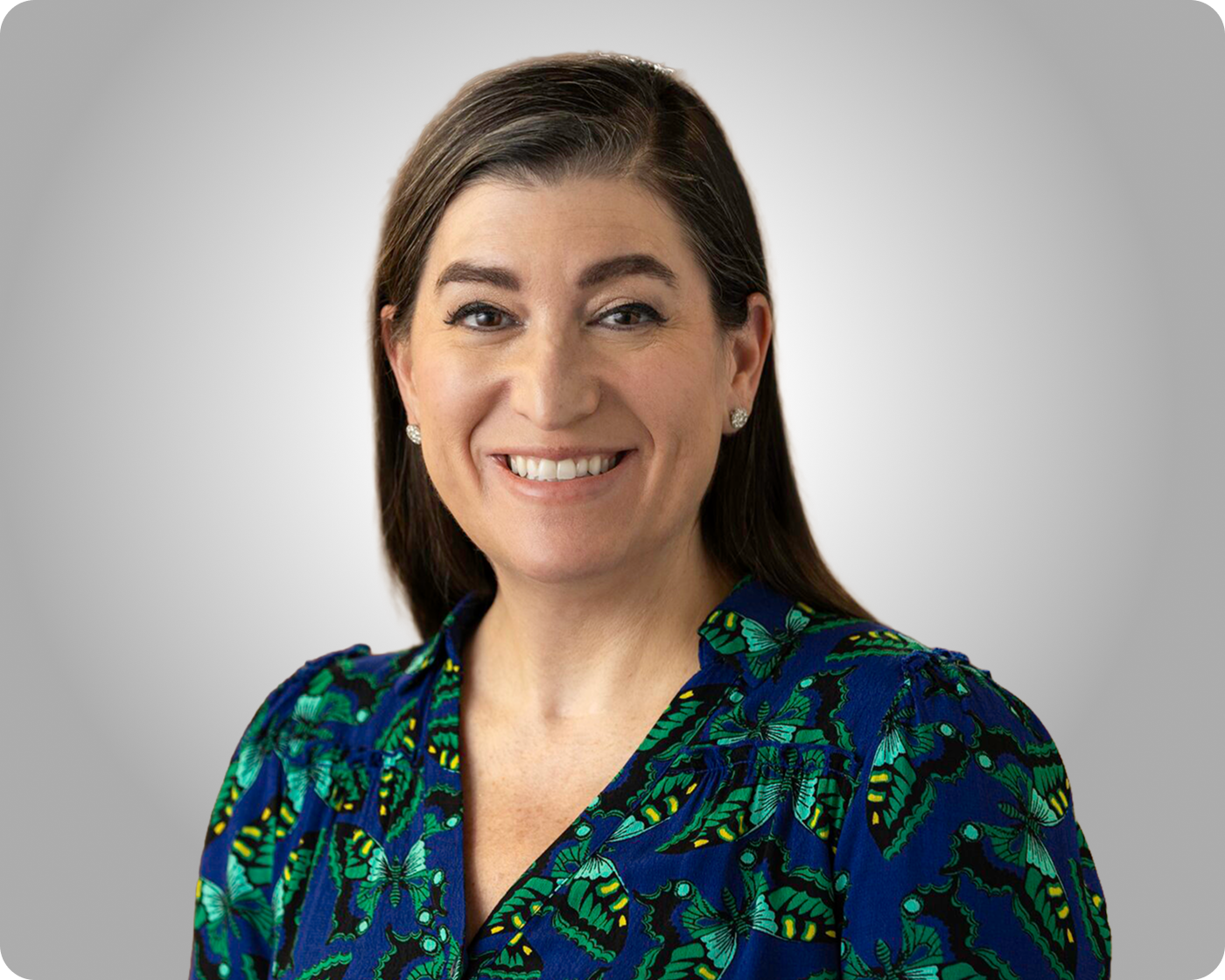 Professional headshot of a smiling woman wearing a blue patterned blouse against a gray background