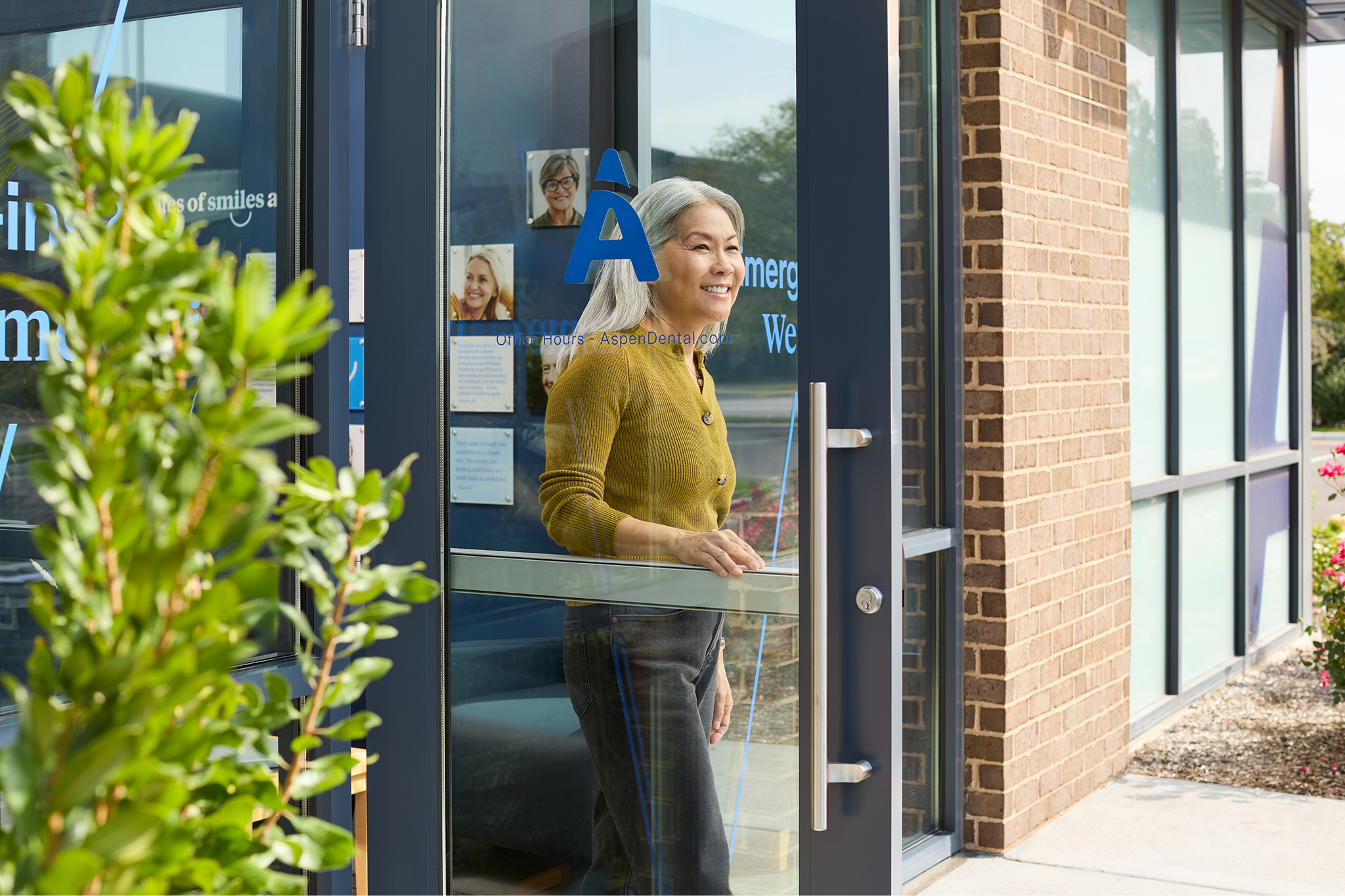 Smiling older woman leaving an Aspen Dental office through a glass door.