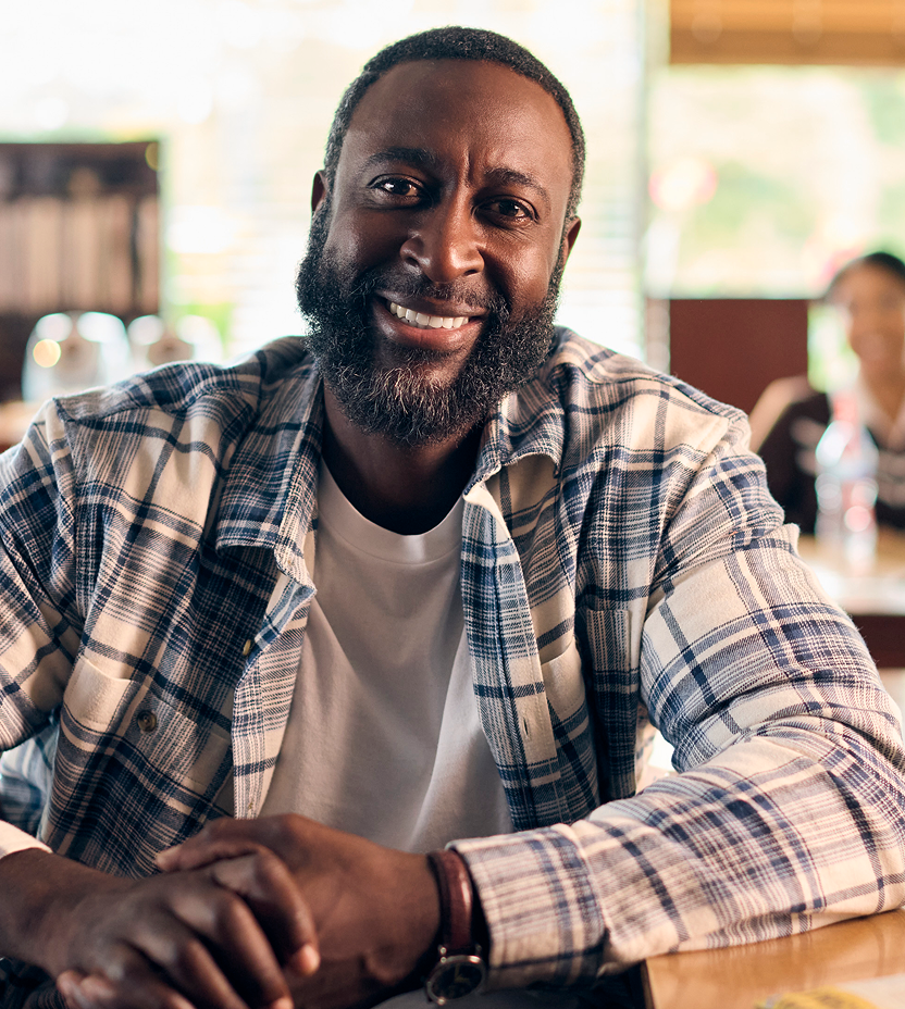 Smiling man sitting at a café table, looking at the camera.