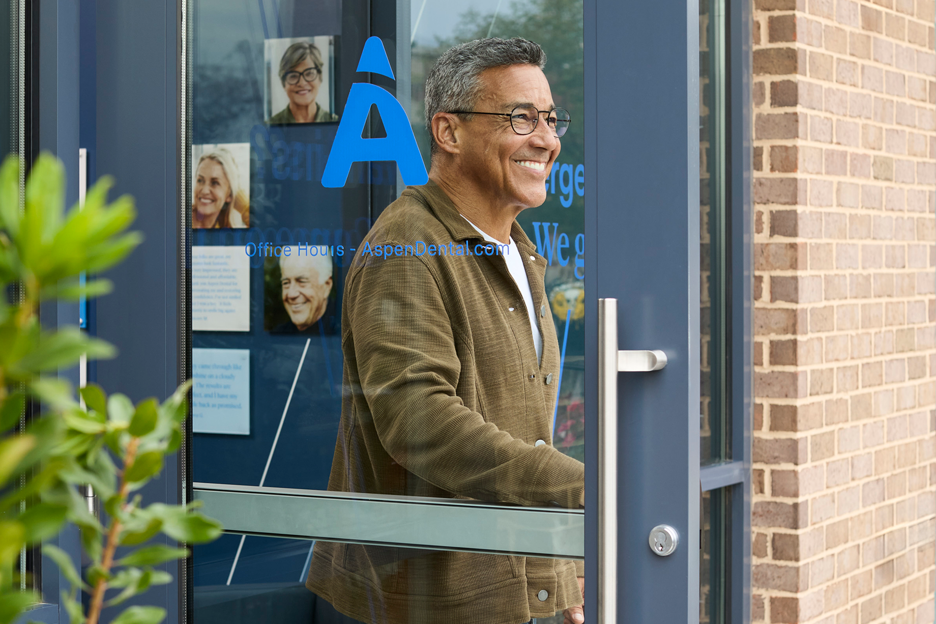 Smiling patient opens the door to leave an Aspen Dental office after their dental appointment.