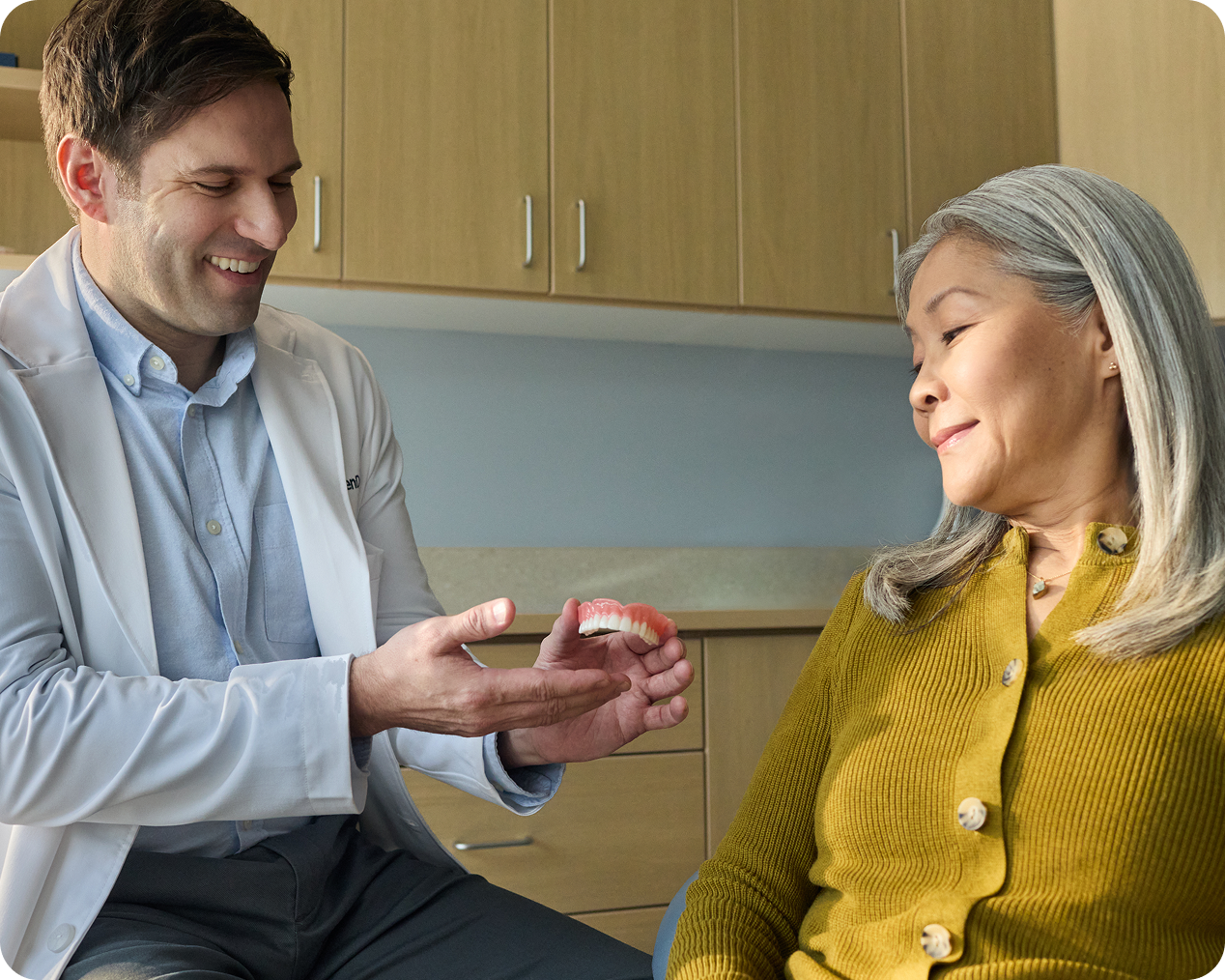 Dentist showing a denture model to a patient during a consultation.