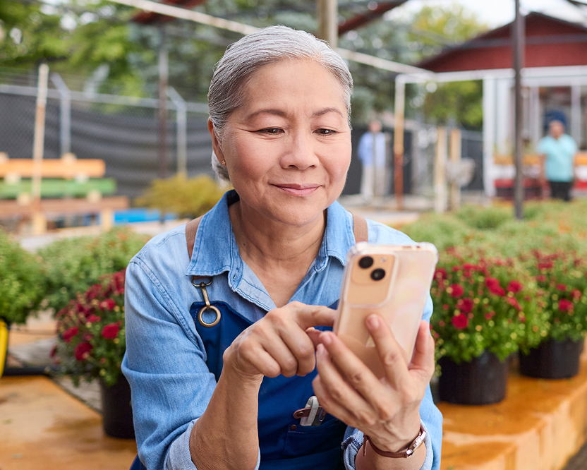 Smiling older woman using a smartphone outdoors, representing scheduling or managing dental care.