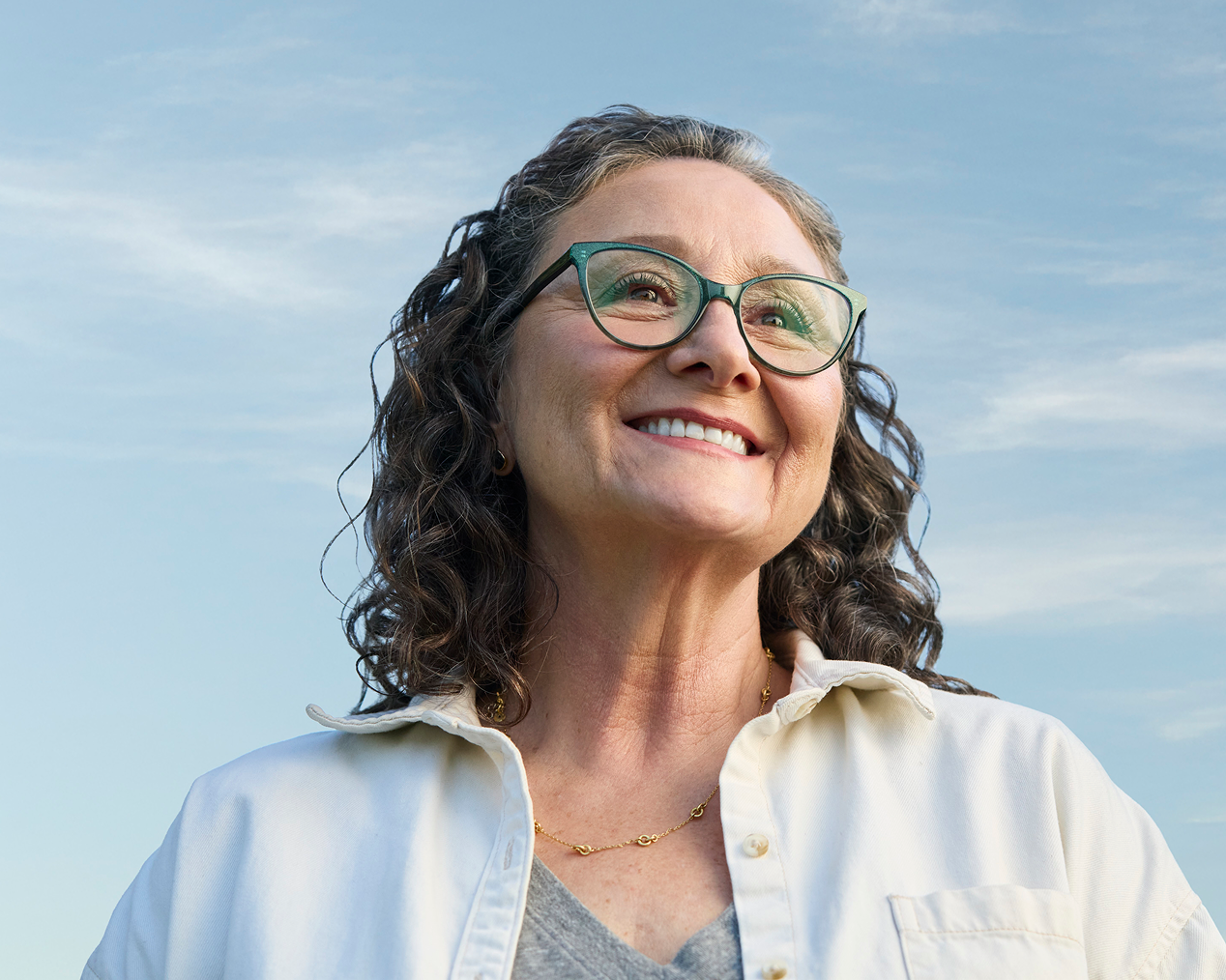 Smiling older woman wearing glasses outdoors, representing confidence after dental treatment.