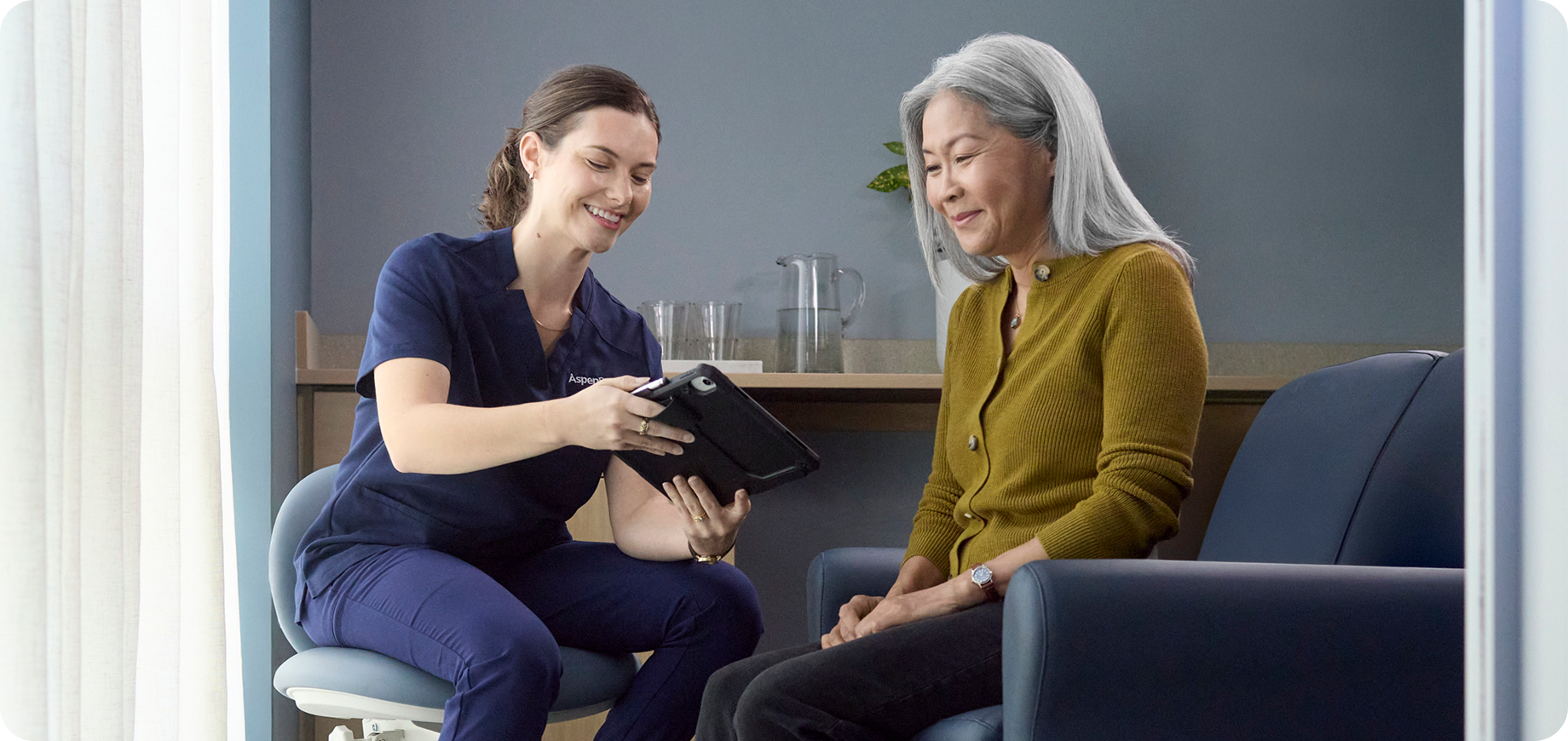 Dental professional reviewing treatment information on a tablet with a senior patient during a consultation.