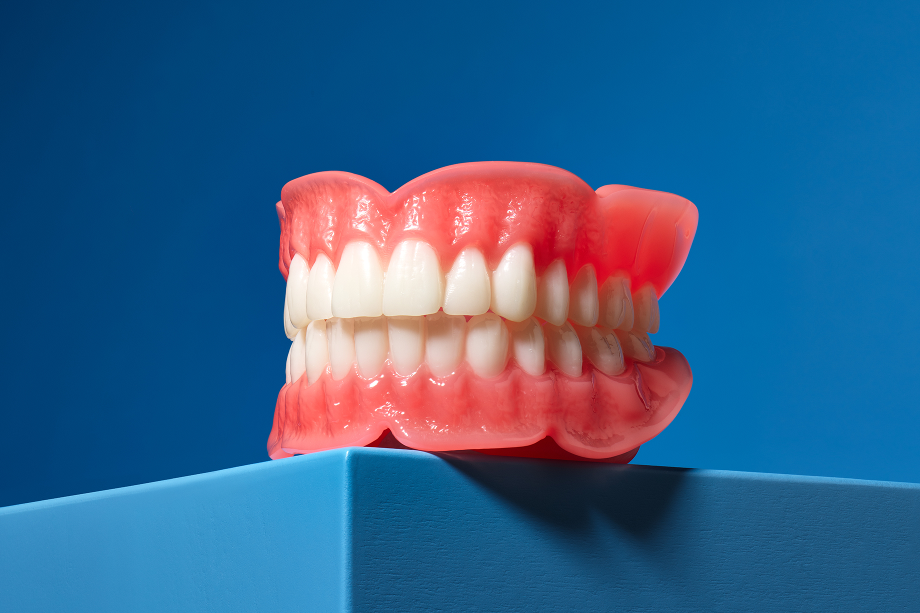 Full upper and lower denture model with pink gum base displayed on a blue surface.