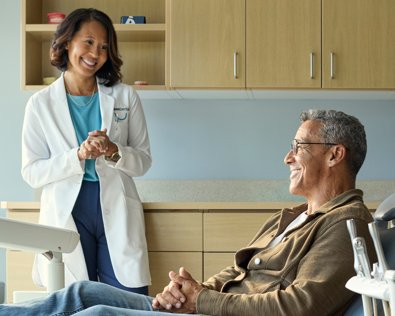 Alt text: A smiling female dentist talking reassuringly with a relaxed male patient in a dental chair during a denture consultation.