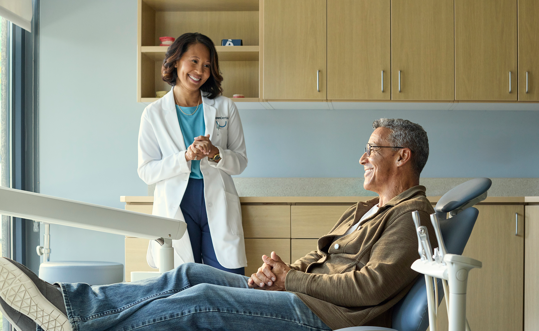 Aspen Dental professional speaking with an older adult man seated comfortably in a dental chair during a visit.