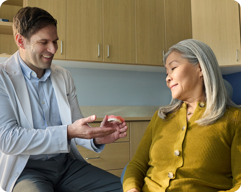 Alt text:
Dentist showing a denture model to a patient during a consultation.
