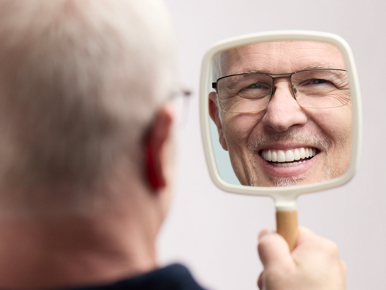  Happy ClearChoice patient admiring her new smile in a hand mirror