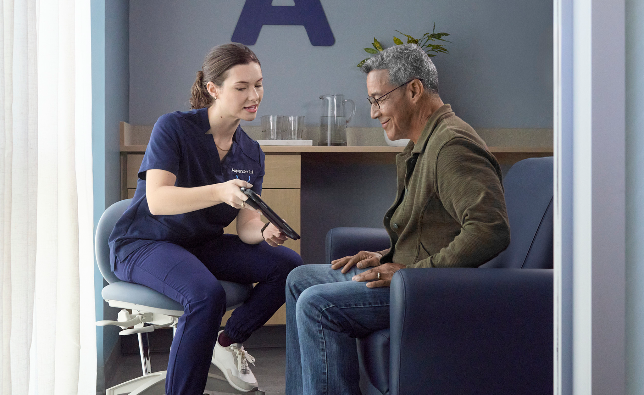 Aspen Dental professional reviewing information on a tablet with an older adult man during a consultation.