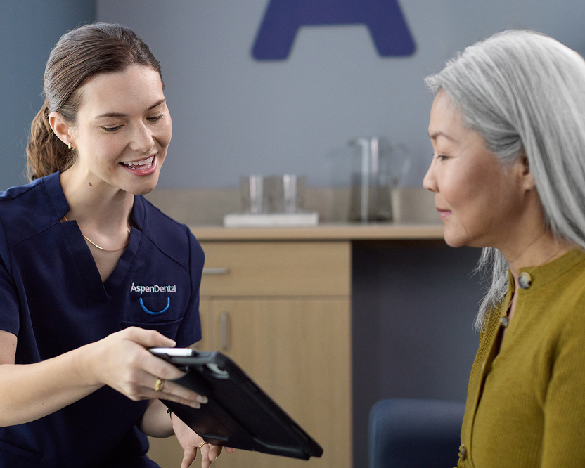 Alt text:
Aspen Dental team member reviewing information on a tablet with an older adult woman during a visit.