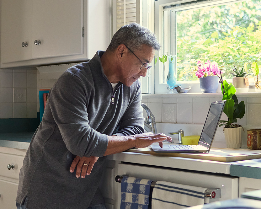 Older adult man using a laptop at home, researching or managing dental care information.