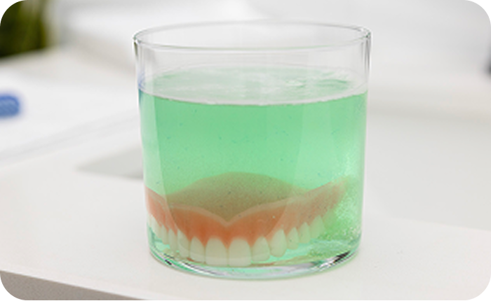 Alt text:
Implant-supported denture soaking in a glass of denture cleaning solution.