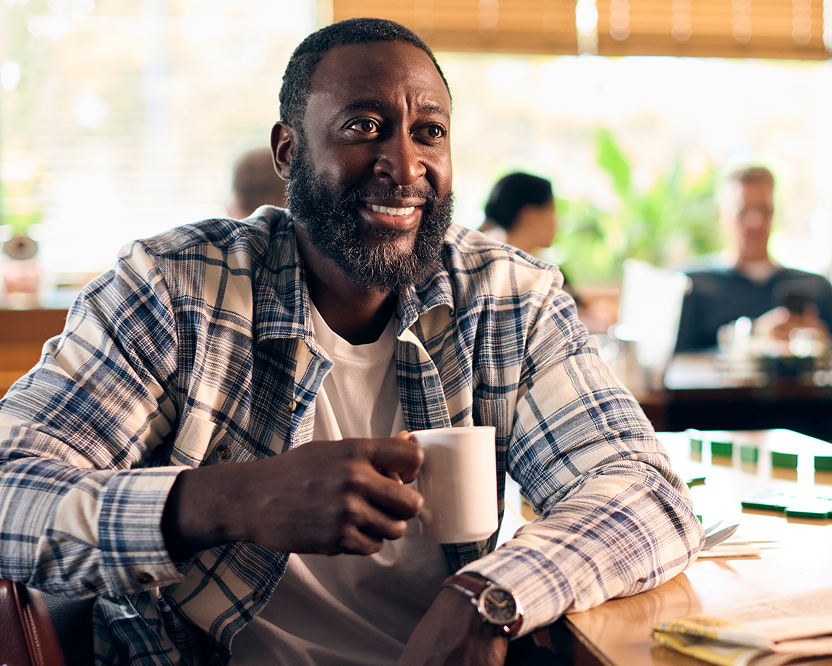 Smiling adult man holding a coffee cup indoors, representing confidence related to dental care.