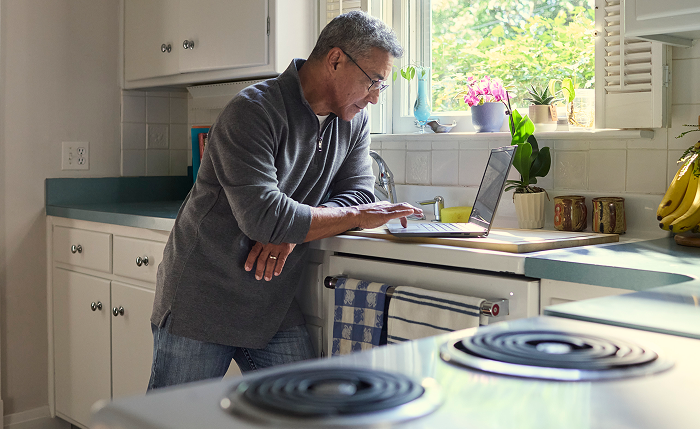 Older man using a laptop at a kitchen counter.