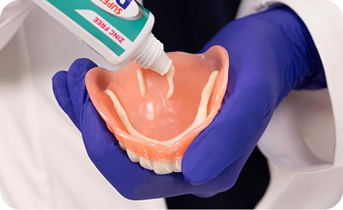 Dental professional applying adhesive to a denture.