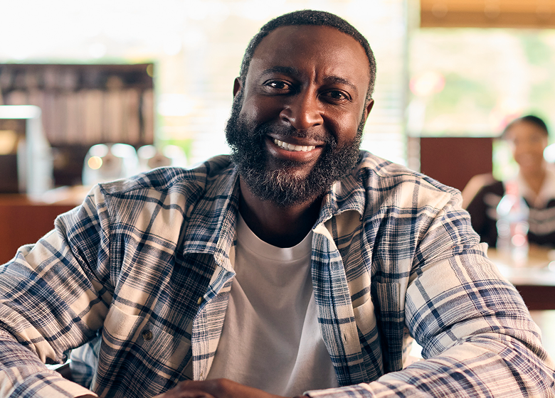 Smiling man sitting at a café table, looking at the camera.