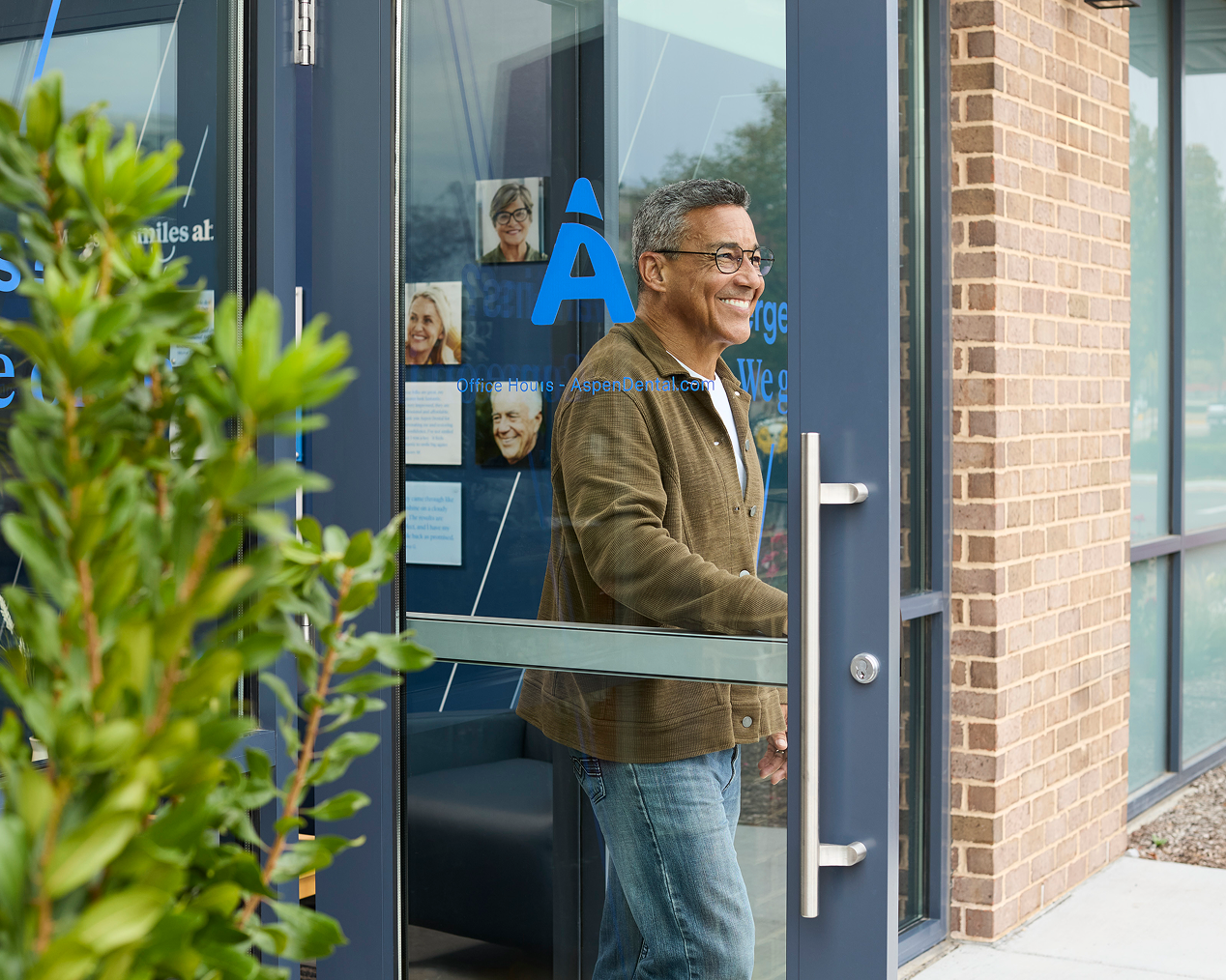 Alt text:
Smiling older man leaving an Aspen Dental office through a glass door.