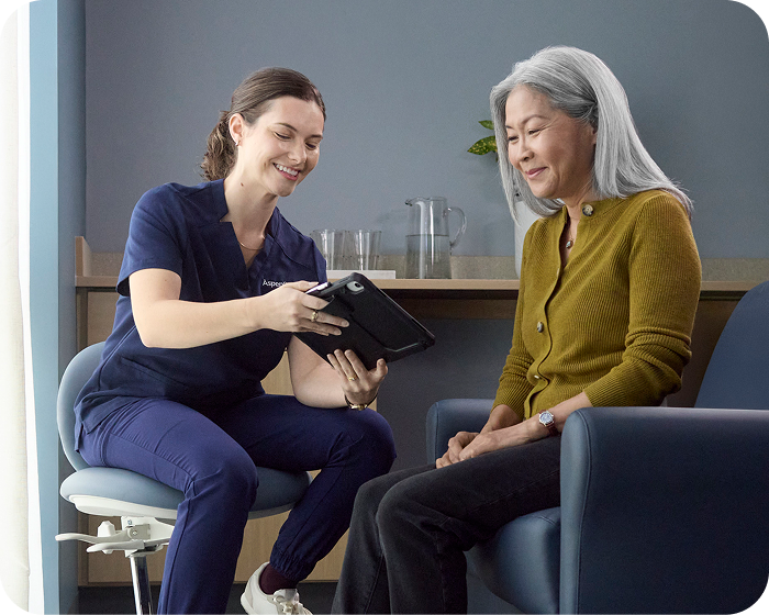 Dental professional reviewing treatment information on a tablet with a senior patient during a consultation.