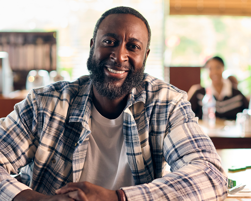 Alt text:
Smiling adult man seated indoors with a relaxed, confident expression, representing confidence related to dental care.