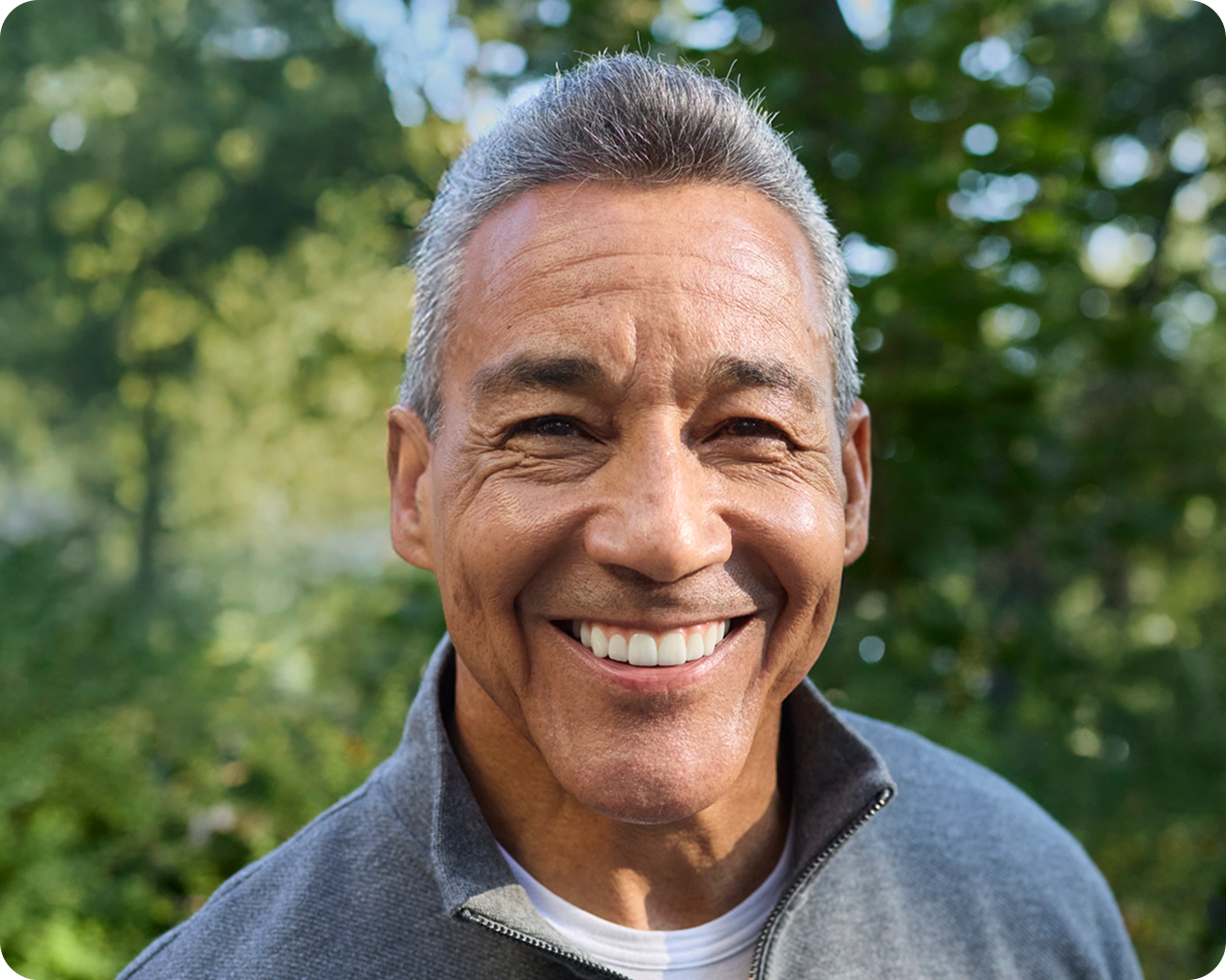 Senior man smiling broadly outdoors, showing off natural-looking dental implants.