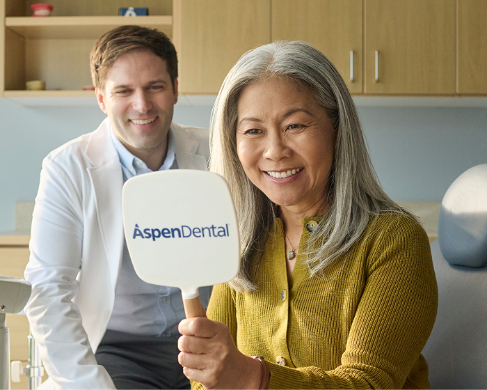 Alt text:
Patient smiling while holding an Aspen Dental mirror during a dental visit.