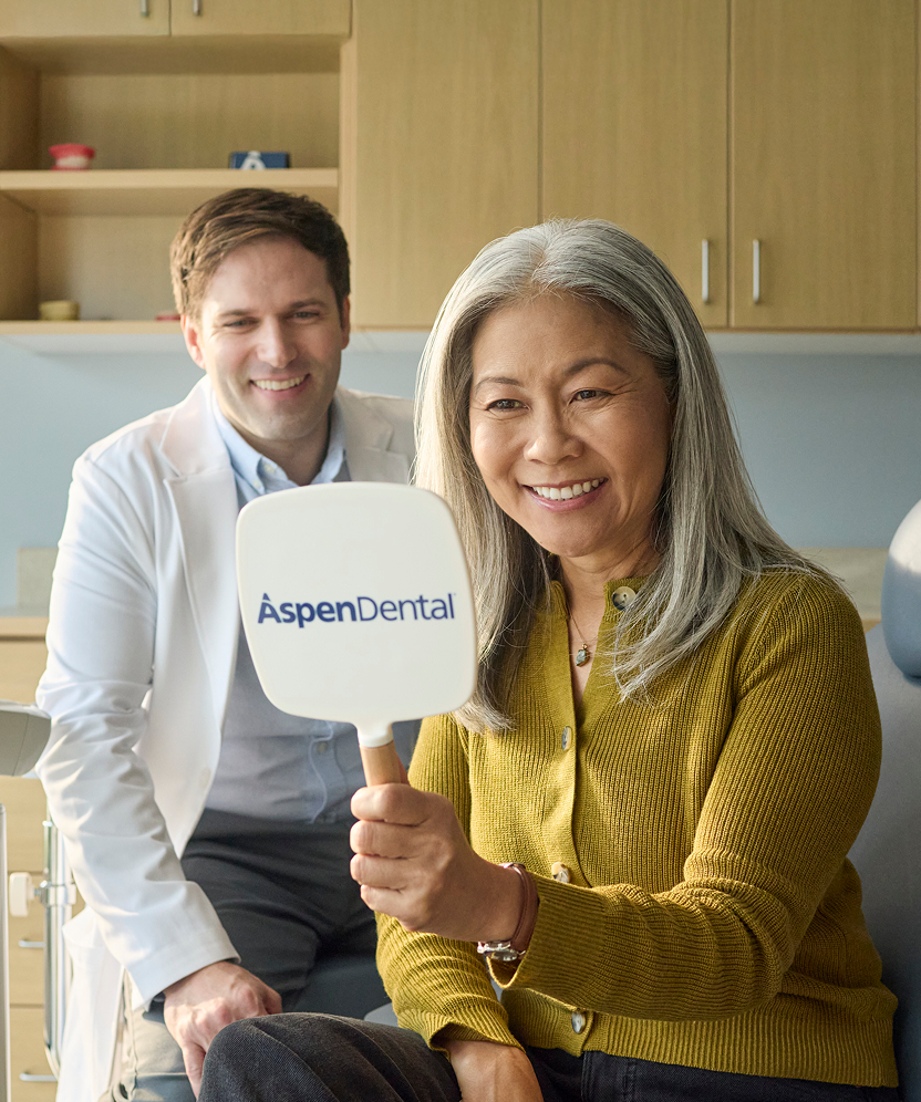 Patient smiling while looking at her teeth in an Aspen Dental mirror.