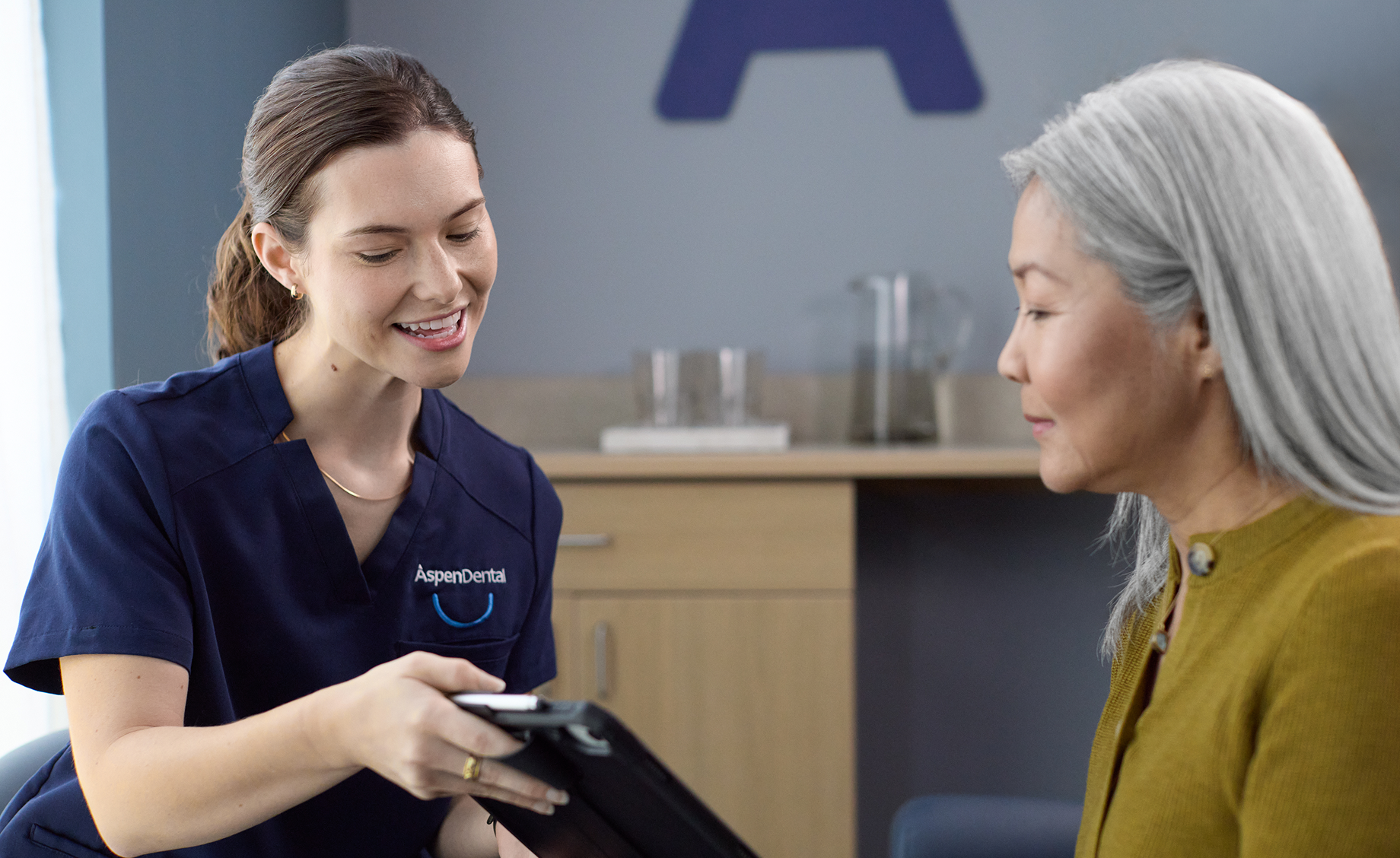 Dental professional showing information on a tablet to an older woman during a dental visit.