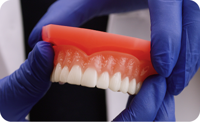 Dental professional holding a denture with gloved hands.
