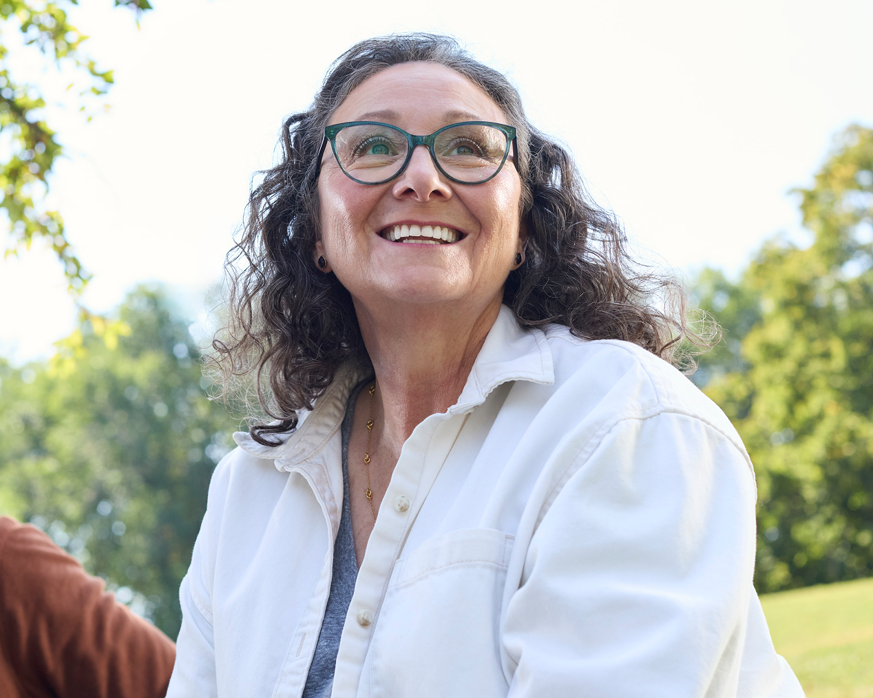 Alt text:
Smiling adult woman wearing glasses outdoors with a confident expression.