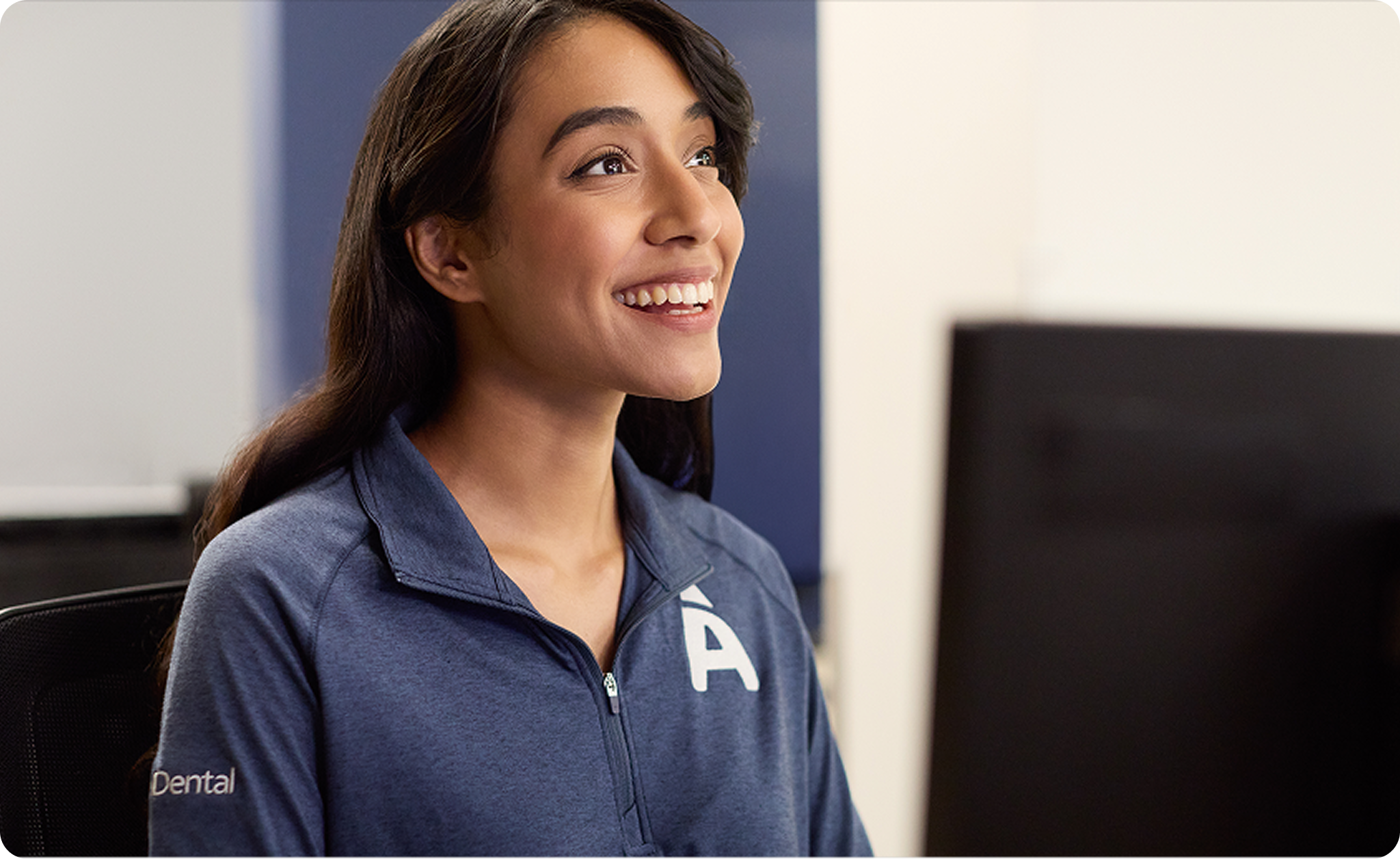 Smiling Aspen Dental team member sits behind a desk with a computer.