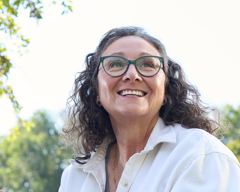 Alt text:
Smiling adult woman wearing glasses outdoors with a confident expression, representing confidence related to dental care.