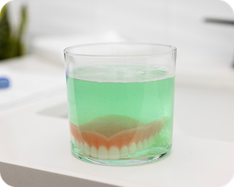 Alt text:
Implant-supported denture soaking in a glass of denture cleaning solution.