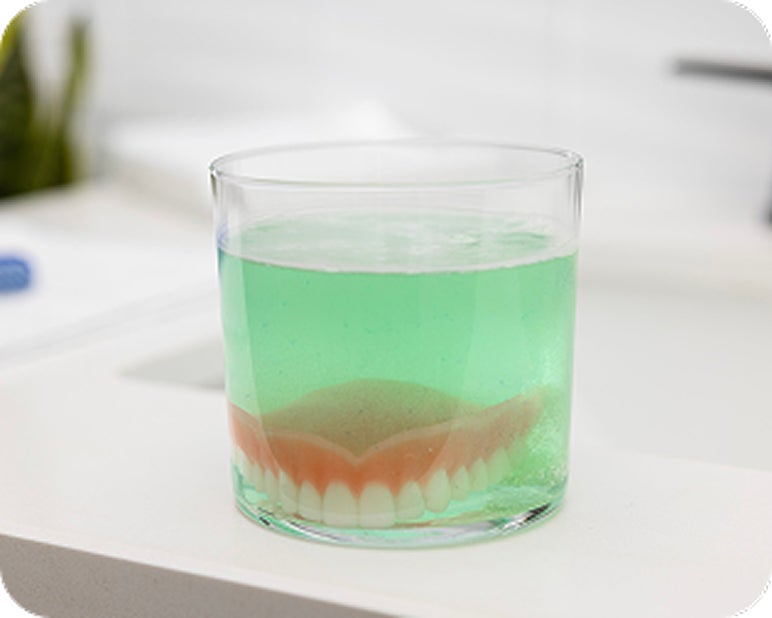 Implant-supported denture soaking in a glass of denture cleaning solution.