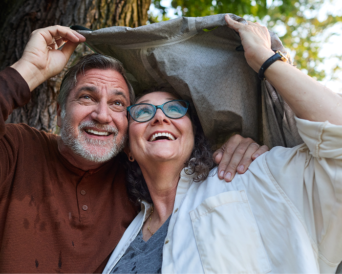 Smiling older couple holding a jacket overhead outdoors and looking up.