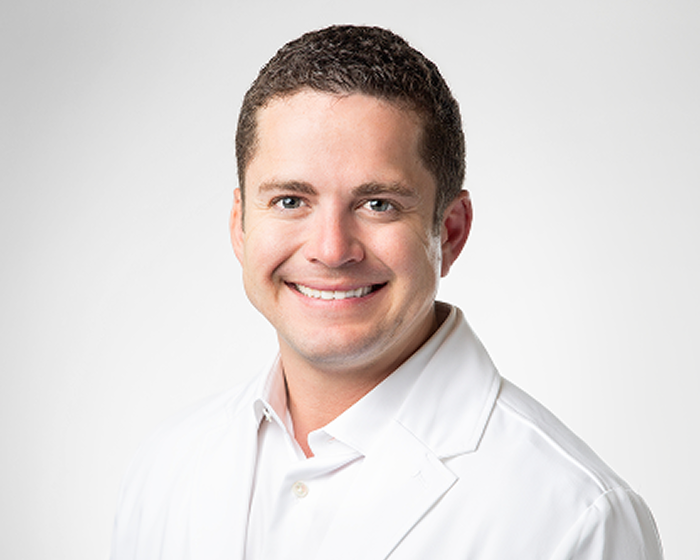 alt text text: Headshot of Dr. De La Rosa, an Aspen Dental dentist, smiling in his white lab coat.