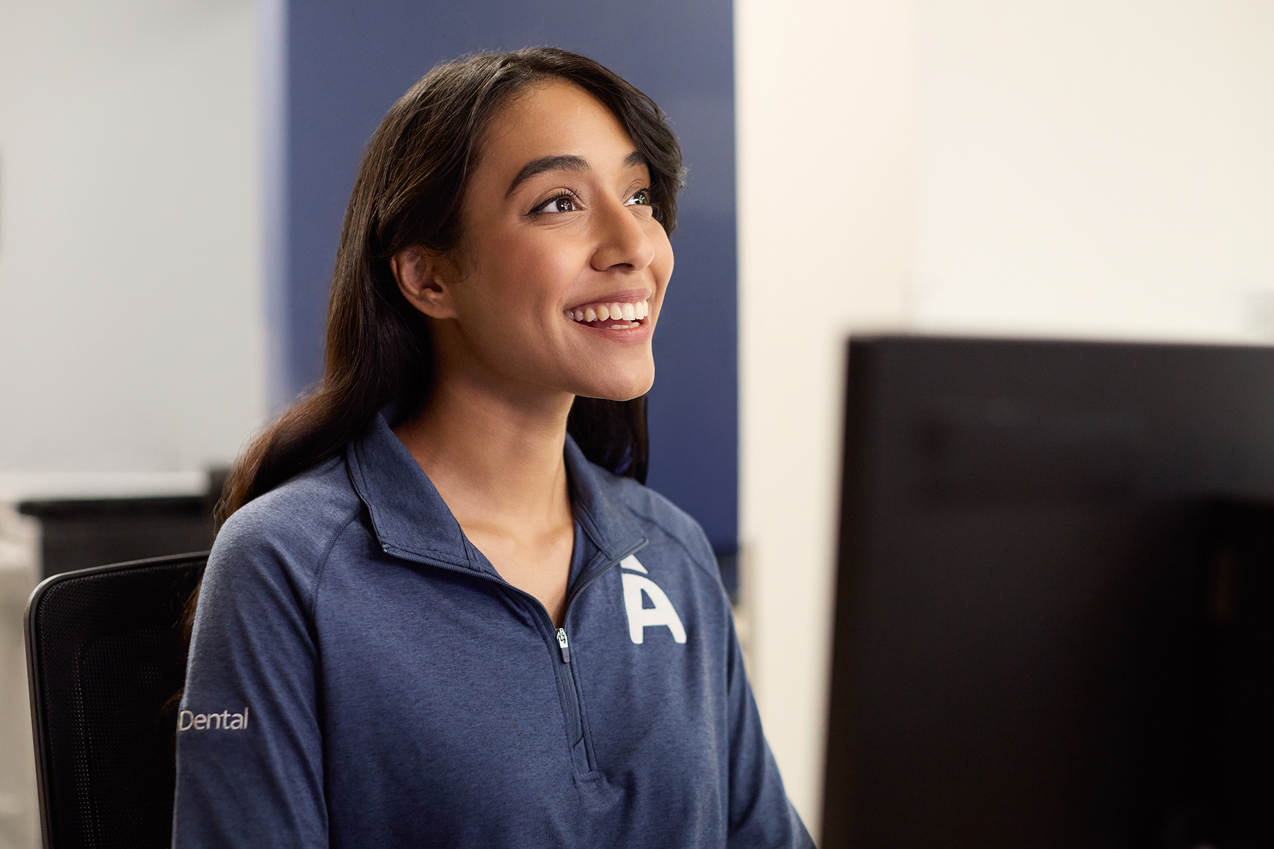 Aspen Dental team member smiles while seated at a desk with a computer.