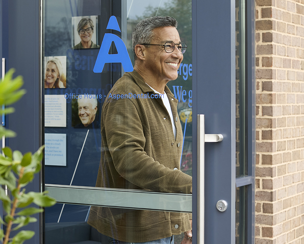 A smiling man enters an office building featuring a prominent 'a' logo on its glass door
